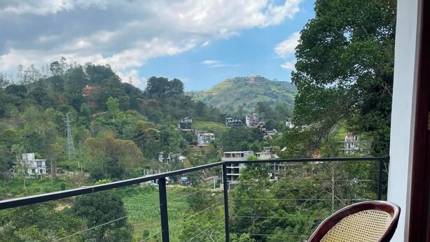 Un balcón con dos sillas y una mesa de madera, con vistas a un paisaje montañoso con casas.