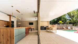 A modern kitchen with a wooden island, a dining area with chairs, and a poolside setting. - Villa Joy Pool Sauna River Escape (Murviel-les-Beziers)