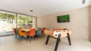 A modern dining area with a foosball table, a TV mounted on the wall, and a large window offering a view of the outdoors. - Villa Joy Pool Sauna River Escape (Murviel-les-Beziers)