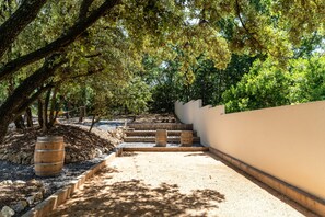 A pathway with wooden steps leading to a white wall, surrounded by trees and a barrel. - Villa Joy Pool Sauna River Escape (Murviel-les-Beziers)