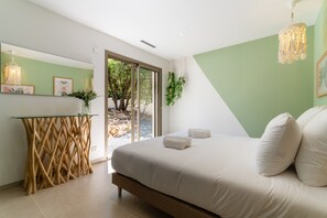 Ein modernes Schlafzimmer mit einem großen Bett, einem Glastisch und Blick ins Freie.