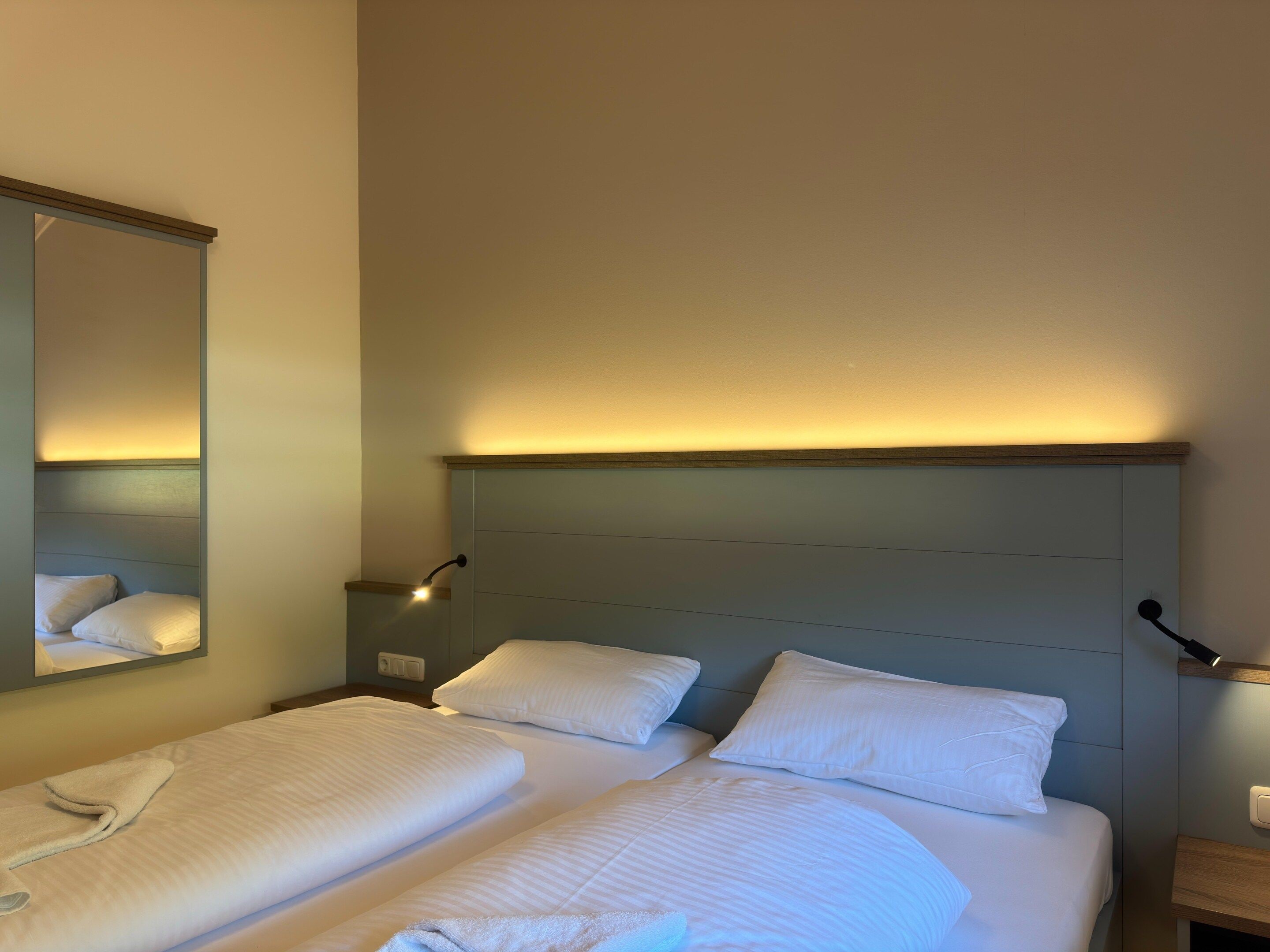 A hotel room with two beds, a bedside table, a mirror, and wall-mounted lamps.