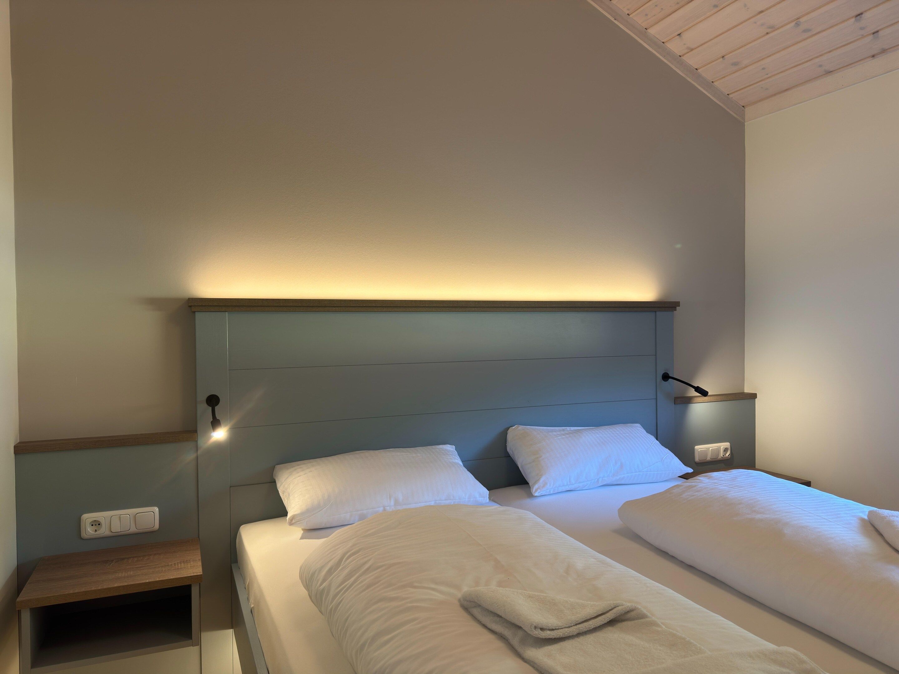 A hotel room with a bed, bedside table, and a wall-mounted light.