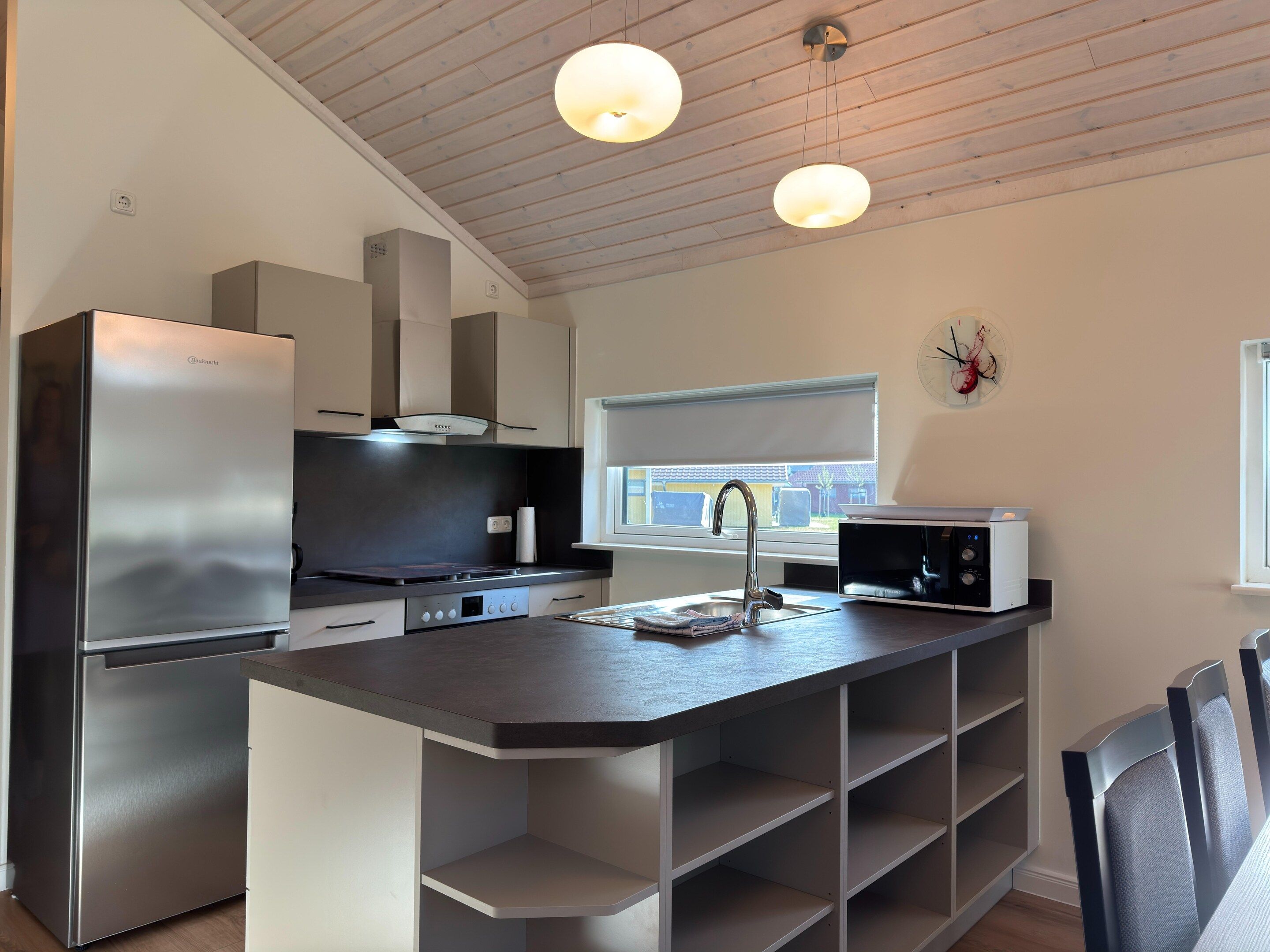 Eine moderne Küche mit einem eingebauten Kühlschrank, einer Mikrowelle und einem Fenster mit Blick ins Freie.