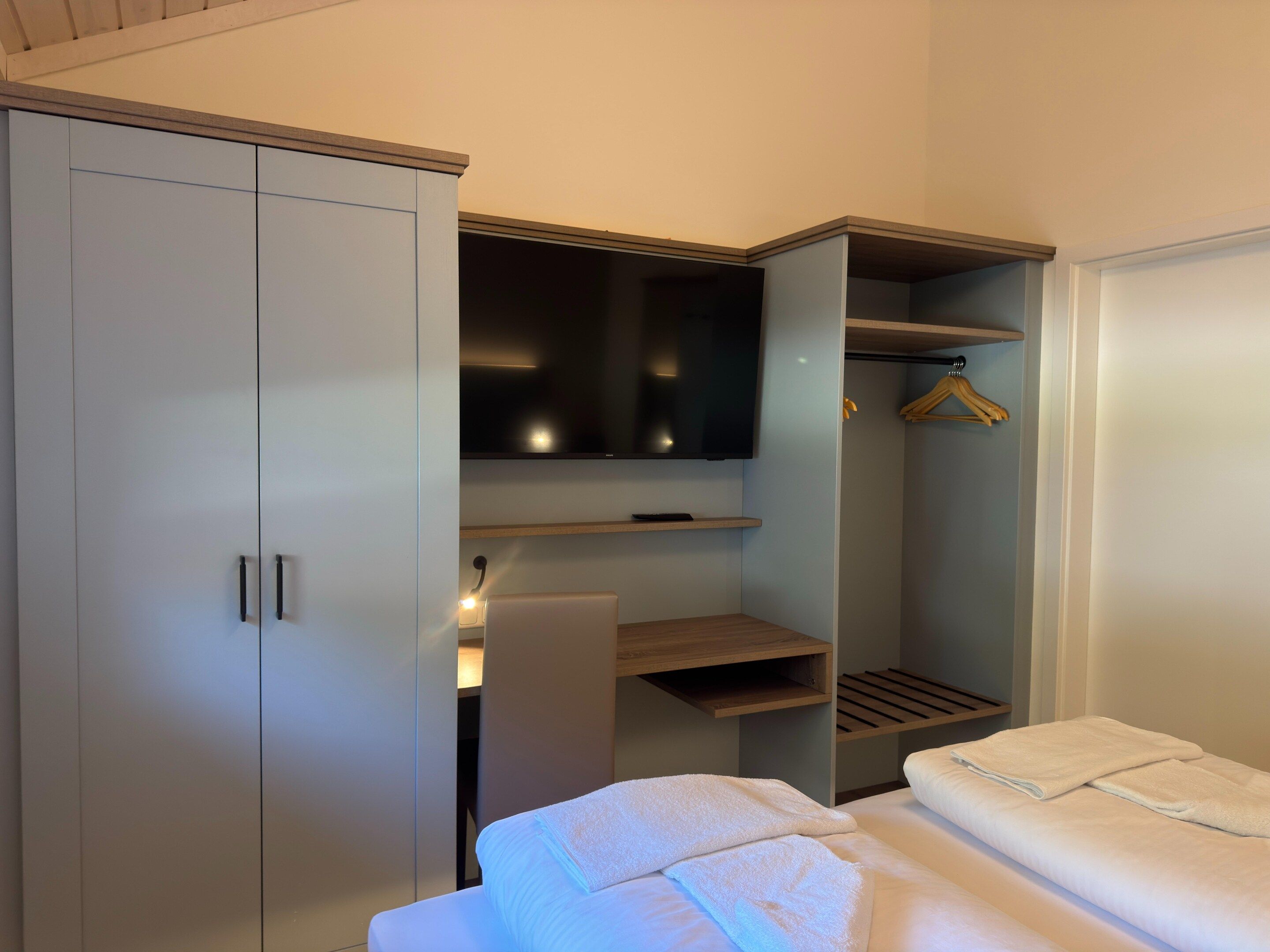 Um quarto com cama, guarda-roupa, televisão e prateleira.