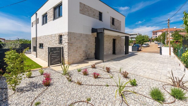 Una casa moderna de dos pisos con fachada de piedra, un camino de acceso y un pequeño jardín.