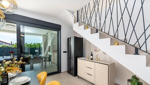 Una cocina moderna con una escalera, un comedor con sillas amarillas y vistas a través de un ventanal.