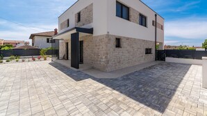 Una casa moderna de dos pisos con fachada de piedra, techo plano y patio empedrado.