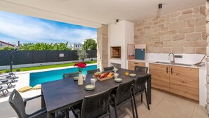 Comedor con vista a la piscina, paredes de piedra y cocina con armarios de madera.