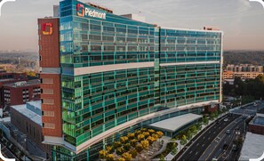 A modern office building with a glass facade, a prominent logo on the side, and a parking lot in front. - The Buckhead Suite (Atlanta)