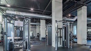 Een sportschool met diverse trainingsapparaten, een bedieningspaneel en een plafond met blootliggende leidingen en luchtkanalen.