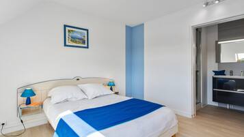 A bedroom with a bed, bedside tables, a nightstand, a blue wall, a door, and a mirror.