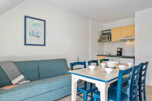 A compact living space with a sofa, a dining table with chairs, a kitchenette, and a framed picture on the wall. - Beautiful 8-person Family Duplex (Île-aux-Moines)