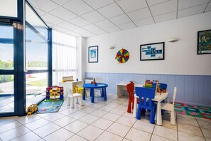 A children's playroom with a large window, colorful play tables, and chairs. - Beautiful 8-person Family Duplex (Île-aux-Moines)