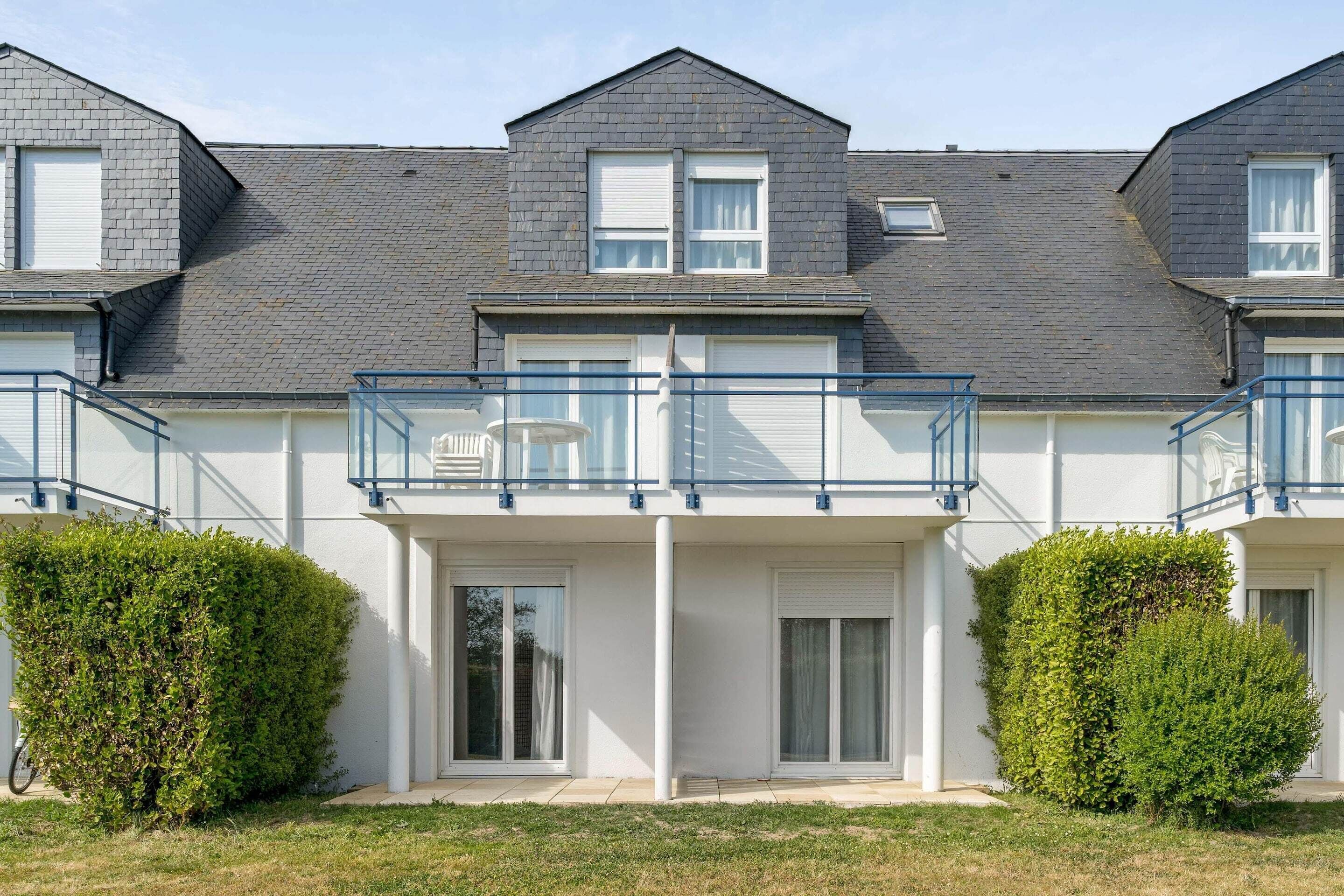 Ein modernes Wohnhaus mit zwei Etagen, einem Balkon, heller Fassade und einem gepflegten Rasen.