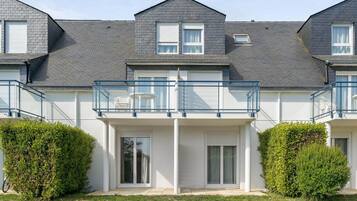A modern two-story residential building with a balcony, white exterior, and a well-maintained lawn.