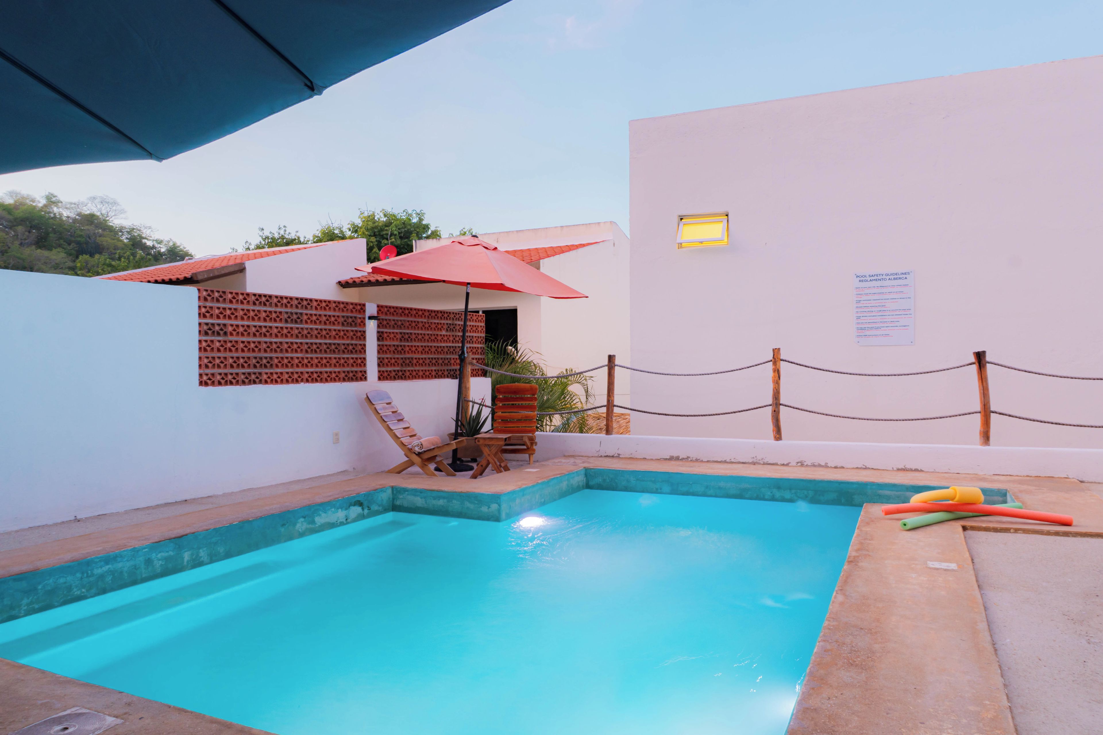 Ein Pool mit einem roten Sonnenschirm, einem Holenzaun und einem Schild an der Wand.