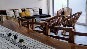Una sala de estar moderna con un sofá, sillas de madera, una mesa de comedor y vistas a través de un ventanal grande.