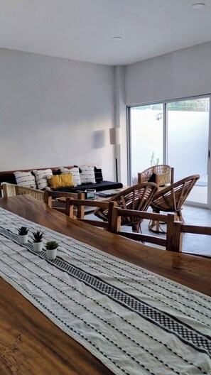 A modern living room with a sofa, wooden chairs, a dining table, and a view through a large window. - Family House in Huatulco, 4 Bedrooms, pool, A.A. Wi Fi, centrally located parking (bahias de huatulco)