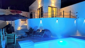 Zona de piscina con un elemento acuático iluminado en azul, sillones de descanso y una escalera que lleva a un nivel superior.
