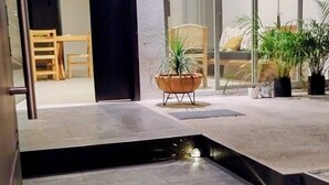 Un interior moderno con suelo de piedra, una pequeña fuente de agua y una zona de estar con una silla y plantas en macetas.