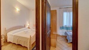 A bedroom with a bed, bedside tables, a nightstand, a wooden door, and a view of another room with a table and curtains. - Spacious Beach Apartment for 6 (Badesi)