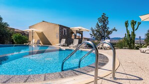 A swimming pool with lounge chairs and umbrellas, a stone building, and cacti in the background. - Spacious Beach Apartment for 6 (Badesi)