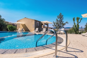 A swimming pool with lounge chairs and umbrellas, a stone building, and cacti in the background. - Spacious Beach Apartment for 6 (Badesi)
