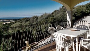 A balcony with a table and chairs, overlooking a landscape with trees and a distant view. - Spacious Beach Apartment for 6 (Badesi)