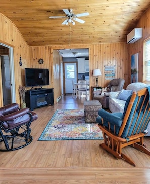 A wooden interior with a ceiling fan, a TV, a rocking chair, a sofa, and a rug.