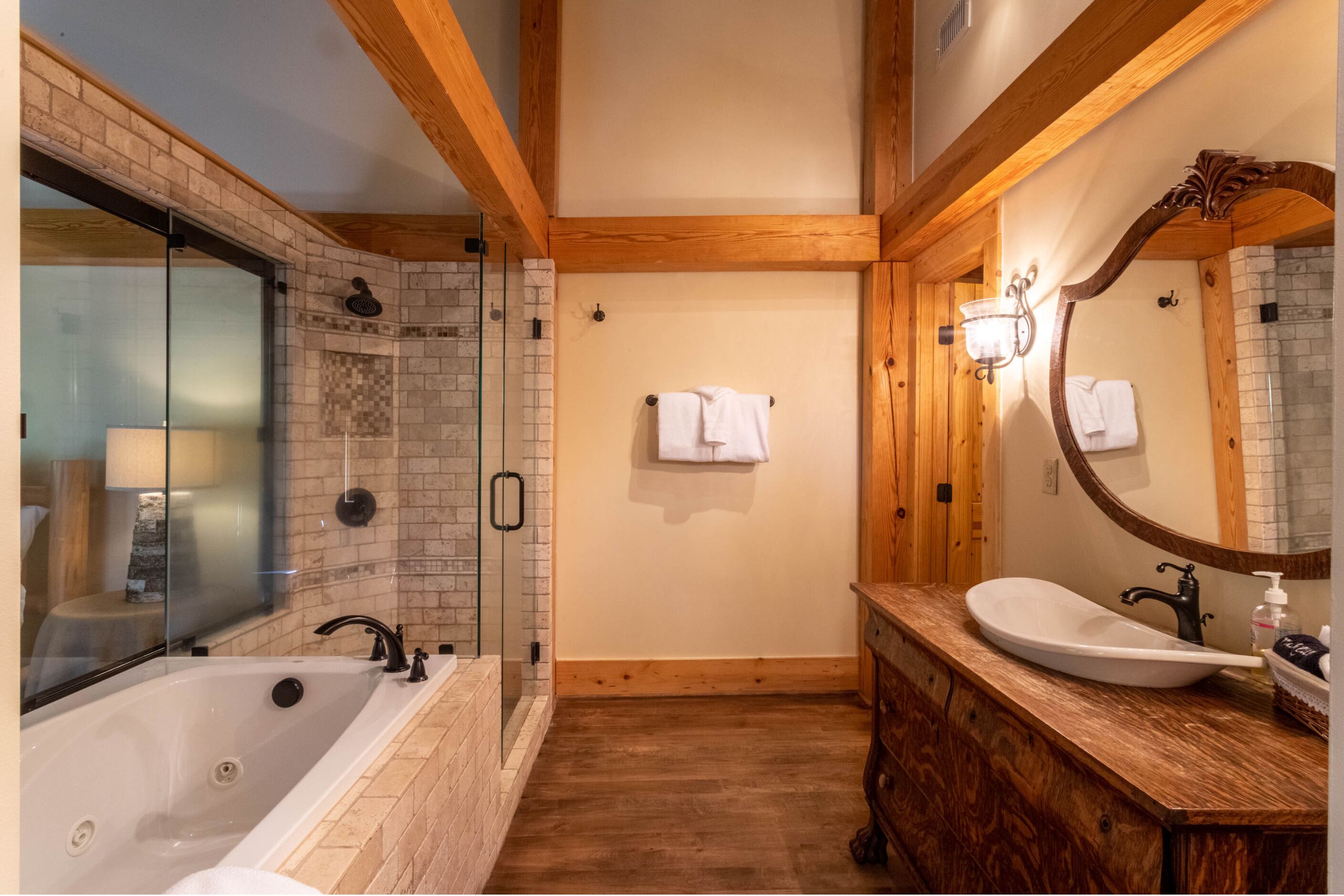 Ein Badezimmer mit einer gläsernen Duschkabine, einer großen Badewanne, einem hölzernen Waschtisch mit Waschbecken und einem Spiegel.