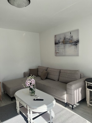 A living room with a sofa, a coffee table, a painting, and a vase with flowers.
