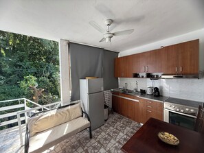 A compact kitchen with wooden cabinets, a refrigerator, a stove, and a dining area with a bench.