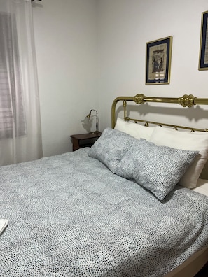 A bed with a patterned bedspread, a bedside table with a lamp, and framed pictures on the wall.