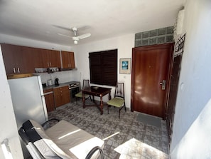 A compact kitchen with wooden cabinets, a dining table, chairs, a ceiling fan, and a tiled floor.