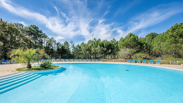 Ein großer, klarer Pool mit blauen Stühlen rundherum, umgeben von Bäumen und einem wolkenlosen Himmel.