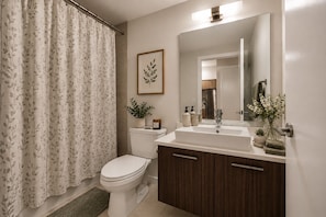 Une salle de bain équipée de toilettes, d’un lavabo, d’un miroir et d’un rideau de douche.
