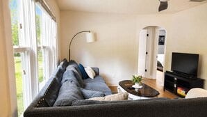 Un salon moderne avec un canapé, une table basse, un meuble pour la télévision et une grande fenêtre.