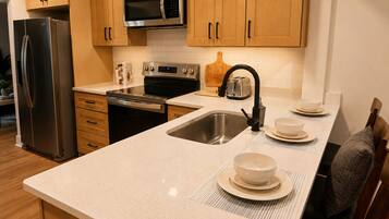A kitchen with stainless steel appliances, wooden cabinets, a microwave, and a sink with a faucet.