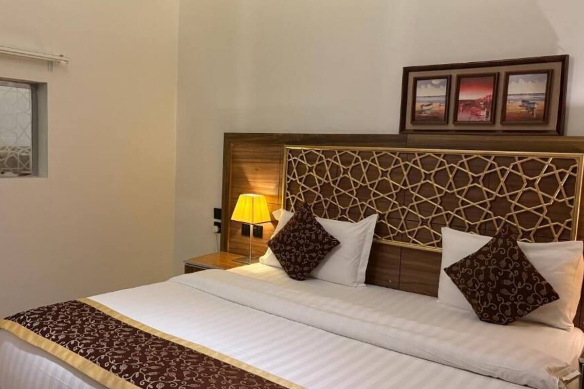 Ein Hotelzimmer mit Bett, Nachttischlampe, Fenster und einem an der Wand befestigten Bilderrahmen.
