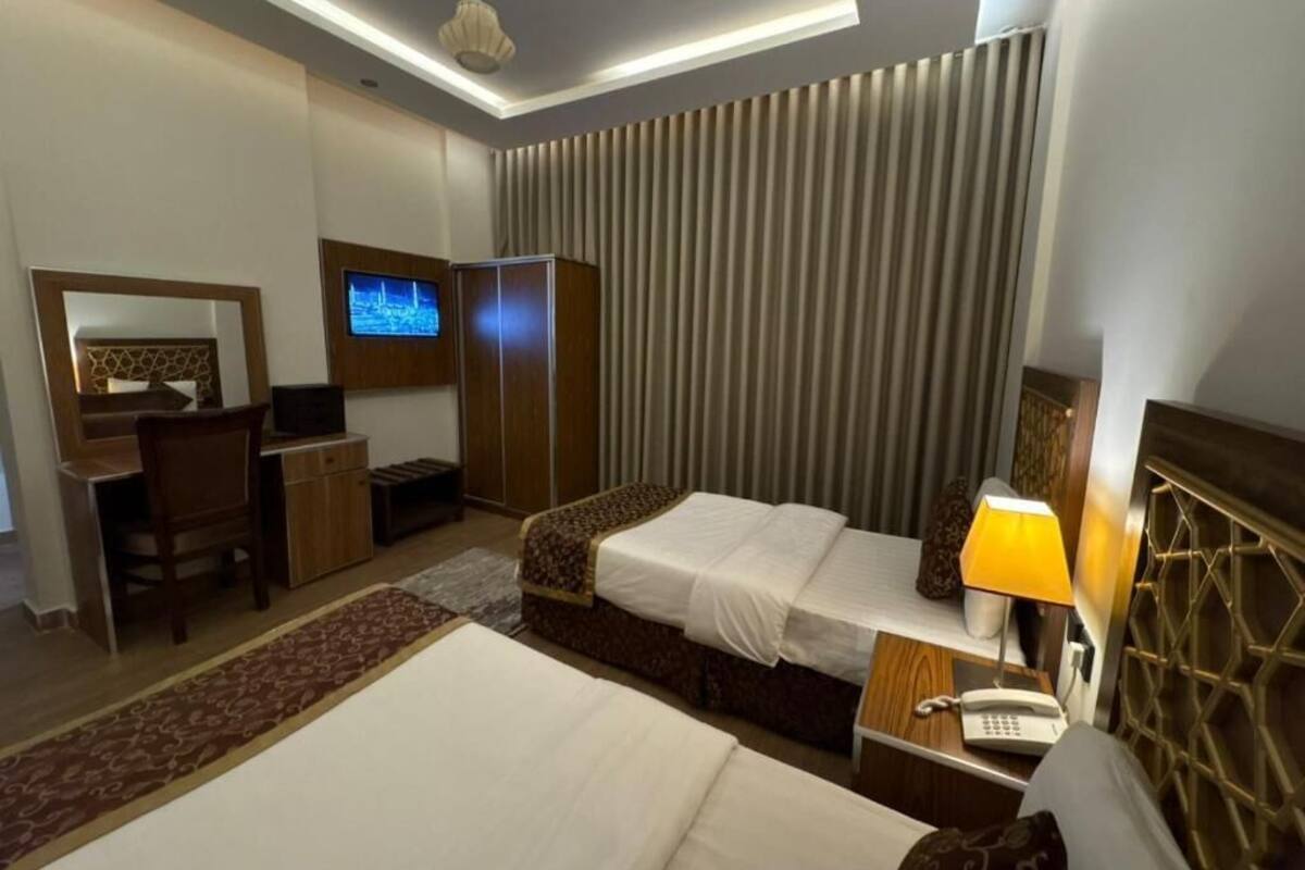 Ein Hotelzimmer mit Bett, Nachttisch, Lampe, Fernseher, Kleiderschrank, Schreibtisch, Stuhl und einem gemusterten Teppich.