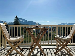 A wooden deck with two cushioned chairs and a table, overlooking a mountainous landscape.