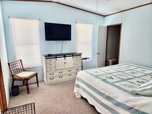 Ein Schlafzimmer mit Bett, Schminktisch, Stuhl und Fernseher an der Wand.