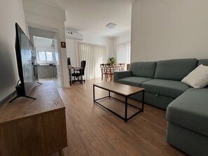 En moderne stue med en sofa, et sofabord og et fjernsyn på et stativ.