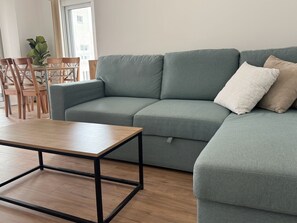 En moderne stue med en grå hjørnesofa, et træsofabord og et spiseområde med træstole og et bord.