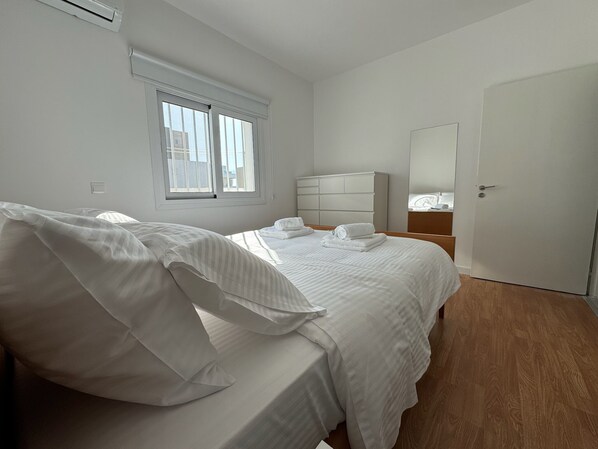 A bedroom with a bed, a bedside table, a wardrobe, a window, and a door.