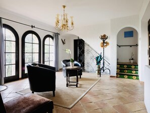 A spacious room with large arched windows, a chandelier, a black leather armchair, a small round table, and a staircase with green steps. - La Torre CostaBravaSi - Pool, BBQ, sea views (Platja d'Aro)