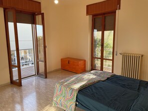 Ein Schlafzimmer mit einem Bett, einer hölzernen Truhe, einem Heizkörper und einer Glastür, die zu einem Außenbereich führt.