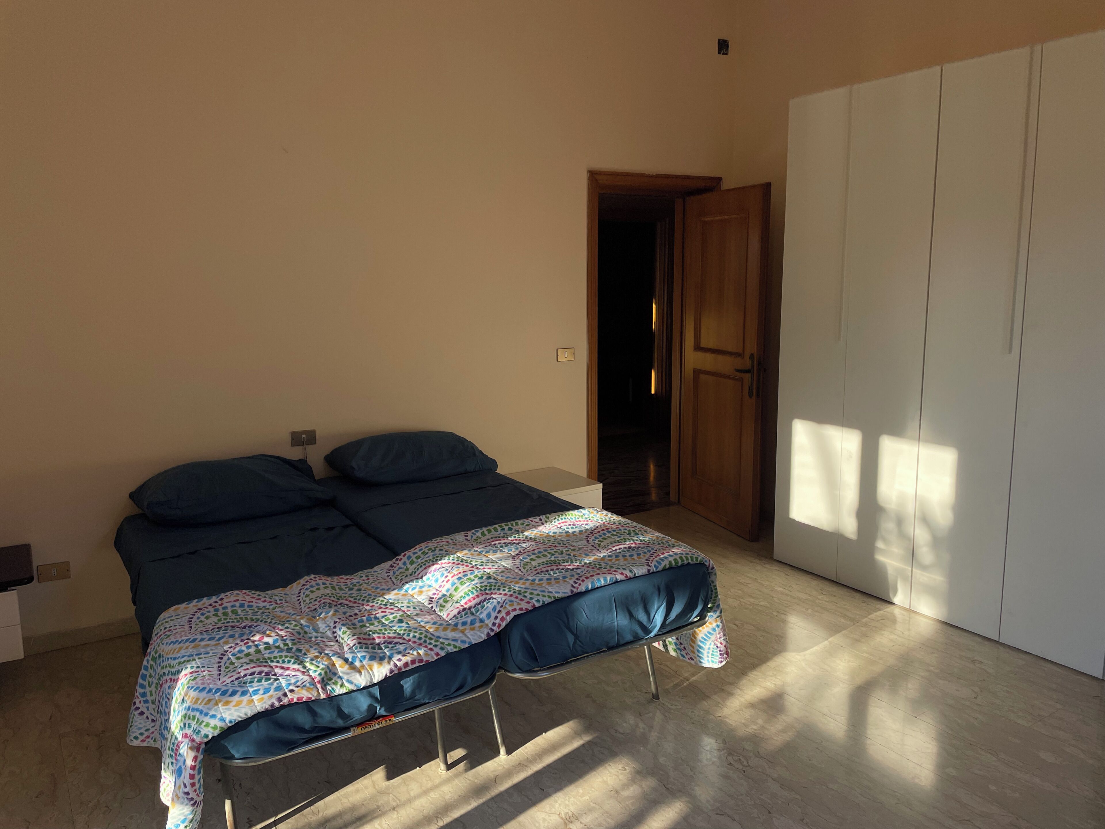 Quarto com cama, guarda-roupa e porta que dá para outro cômodo.