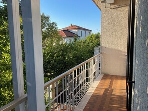 Uma varanda com guarda-corpo de metal, piso de tijolos e vista para um edifício com telhado vermelho.